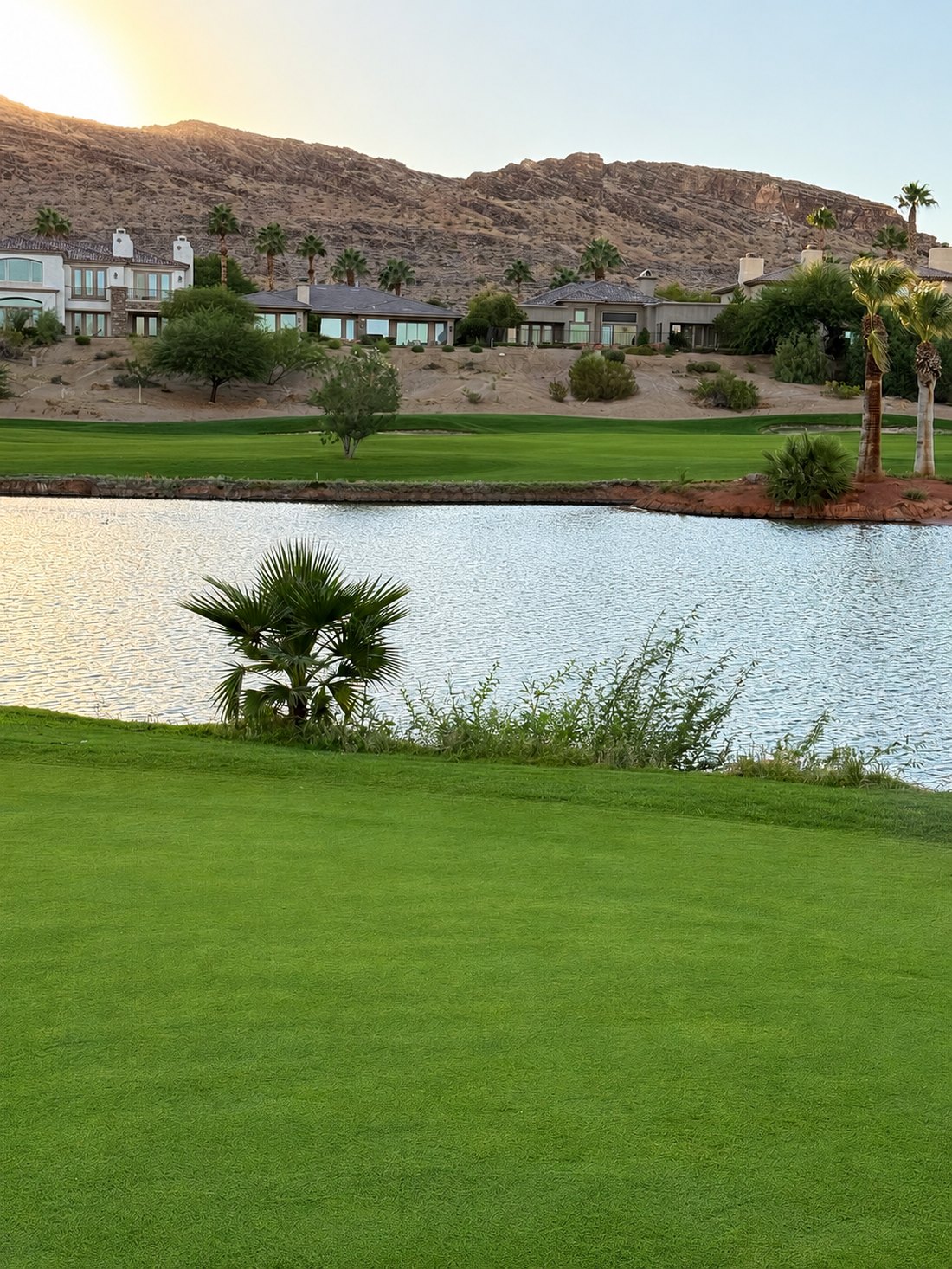 Golden-hour view across a Red Rock Country Club fairway and lake toward custom homes and the desert mountains at sunset