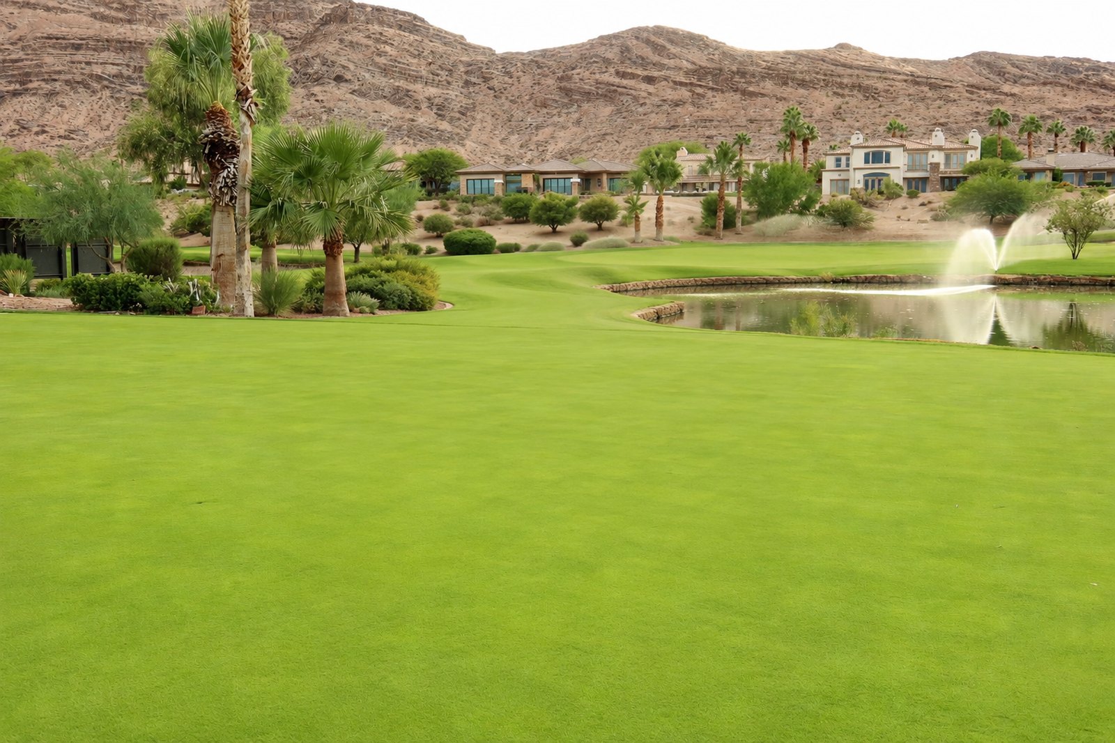 A lush green Red Rock Country Club fairway with a fountain pond, palm trees, custom Summerlin homes, and the rugged Red Rock mountains rising behind