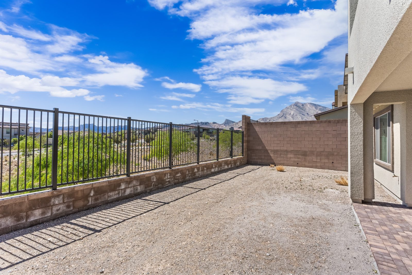 Covered patio and paver deck with a wrought-iron view fence and open desert behind