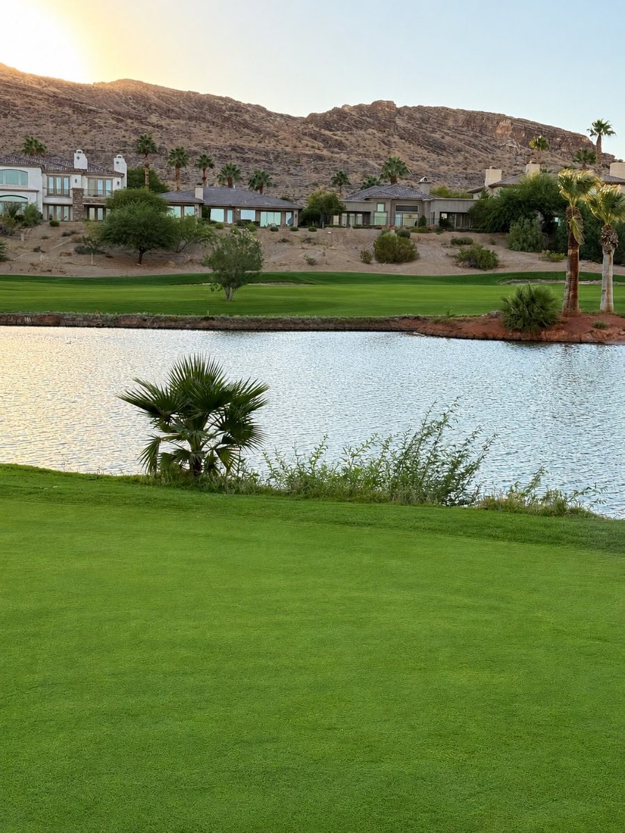Golden-hour view across a Red Rock Country Club fairway and lake toward custom homes and the desert mountains at sunset